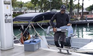 Man carrying a lightweight Momentum M10 electric outboard on a dock beside a boat.
