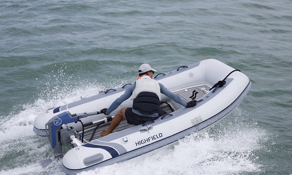 Man driving a Highfield inflatable boat at speed using a Momentum M10 electric outboard on open water.