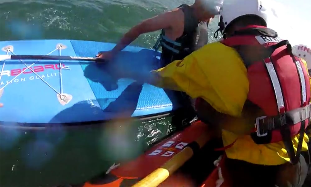 RNLI lifeboat crew assist Mark Parker, a paddleboarder in distress, during a sea rescue.