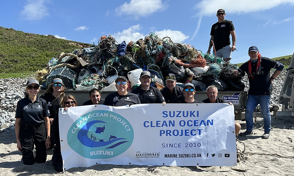 Team of Suzuki Marine volunteers standing on a beach in front of a trailer loaded with marine debris collected during a coastal clean-up.