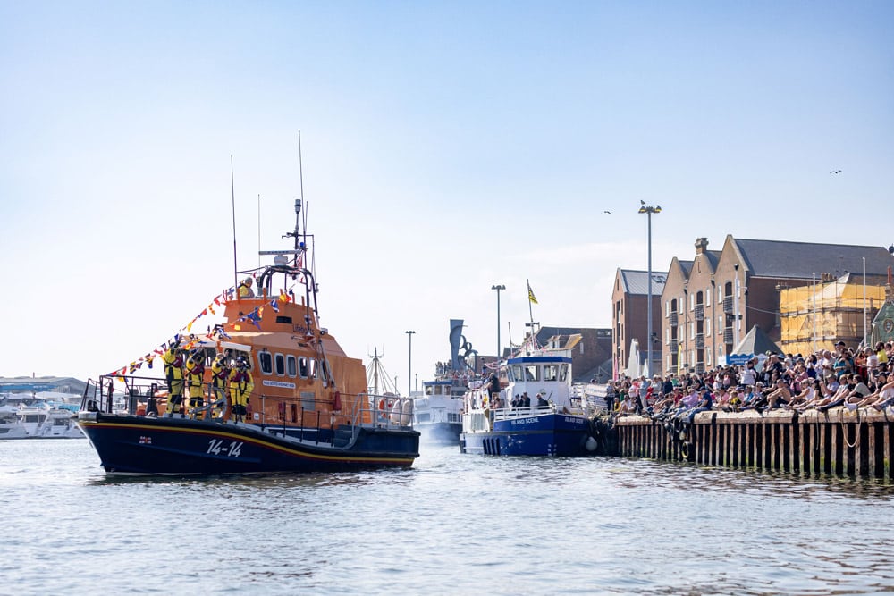A Trent all-weather lifeboat taking part in the flotilla as crowds gather Poole Quay. Flotilla at Poole RNLI Lifeboat Festival - 2024