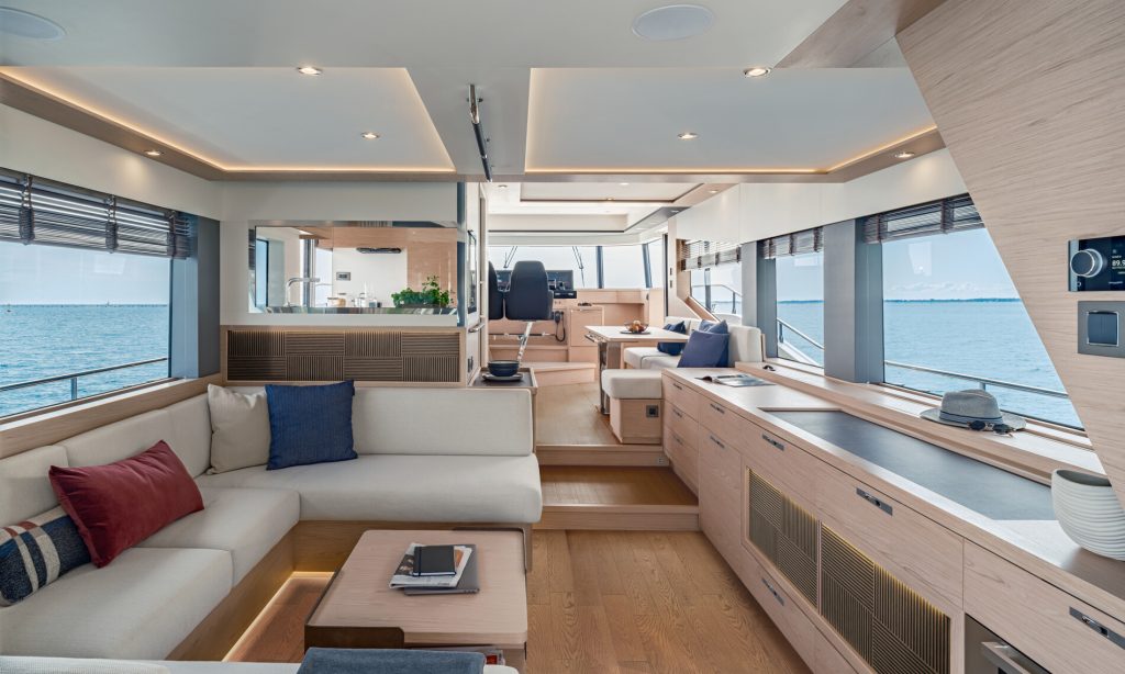 Spacious main saloon of the BENETEAU Grand Trawler 63 with panoramic windows, light oak cabinetry, and open-plan seating leading to the helm.