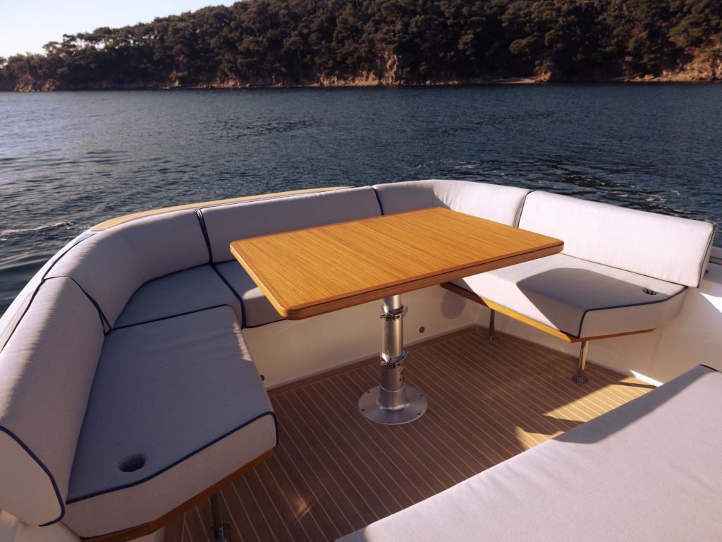 Aiata Wayfinder 38 aft deck with U-shaped seating and teak dining table overlooking calm coastal waters.