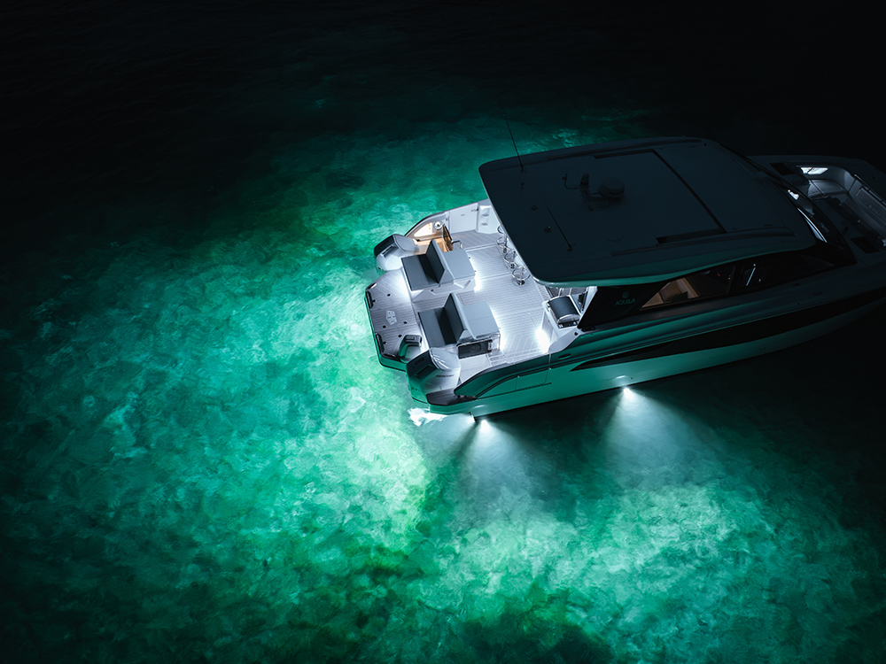 Aquila 46 Coupe at night with bright underwater lights illuminating turquoise water around the aft deck.