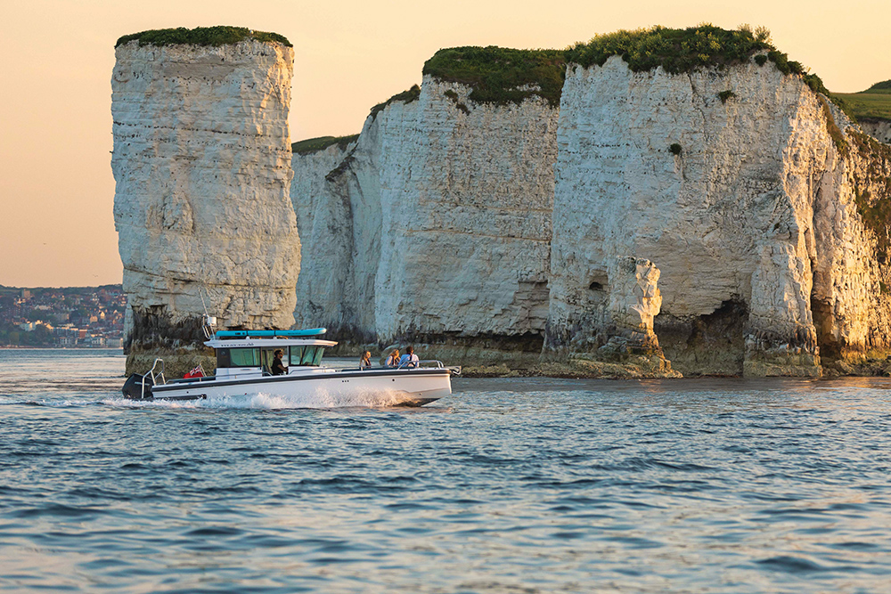 Axopar boat cruising past the white chalk cliffs at Old Harry Rocks in calm evening light.