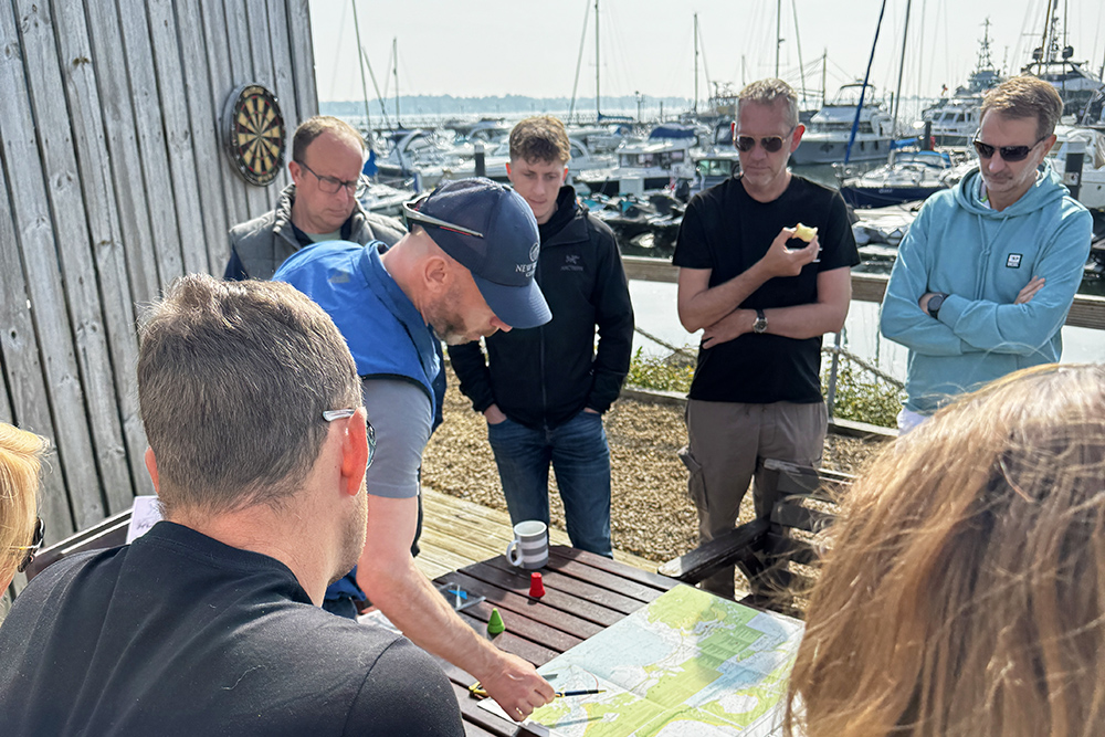 Instructor briefing a group of learners around a chart table at the marina.