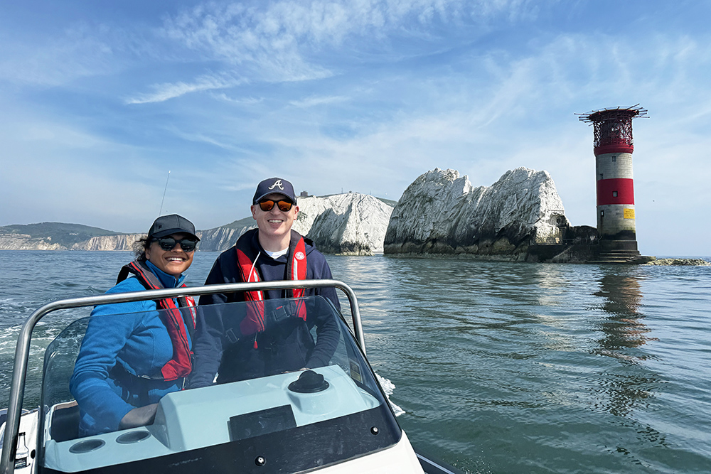 An instructor providing training on a small boat approaching The Needles and its red and white lighthouse on a calm, bright day.