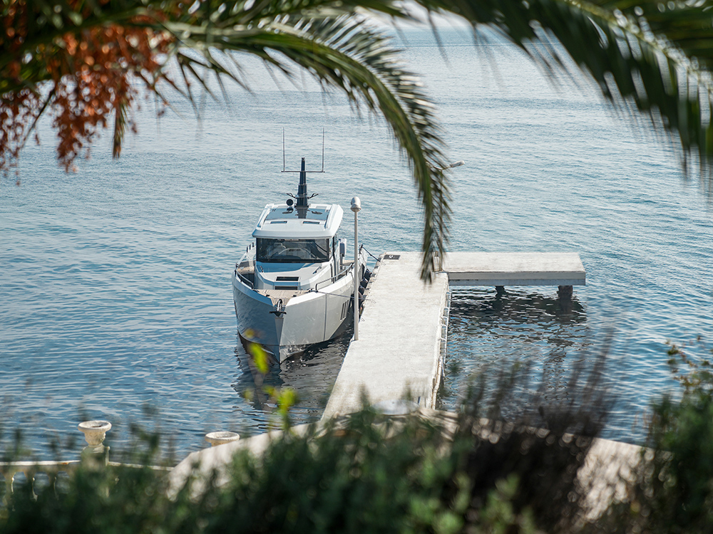 XO EXPLR 44 moored at a quiet waterfront jetty, framed by palm leaves.